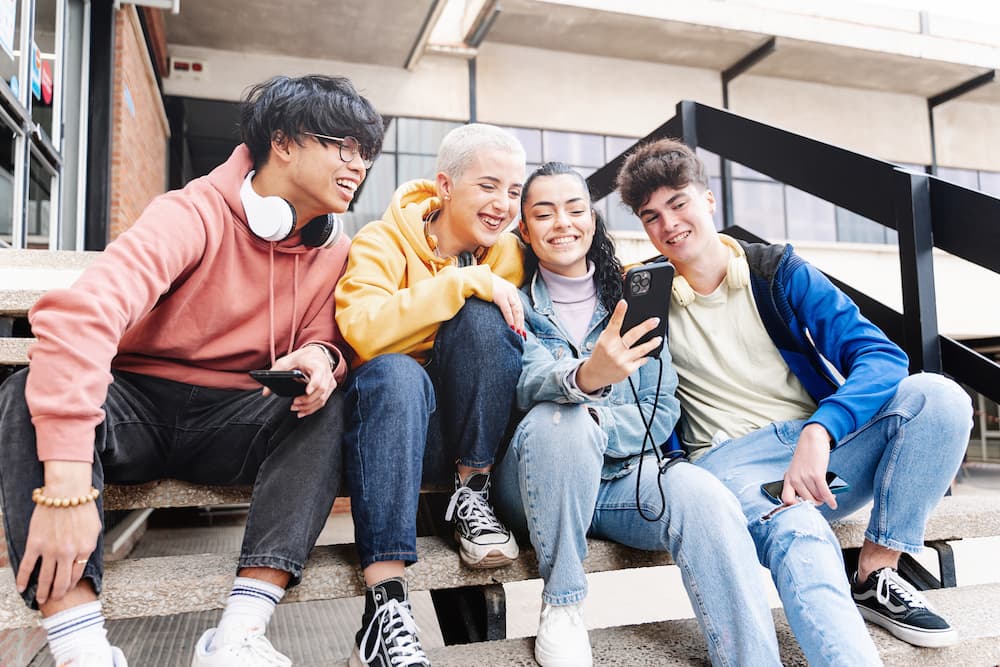 Symbolbild Gen Z und Alpha, lächelnde junge Menschen, die auf ein Smartphone blicken