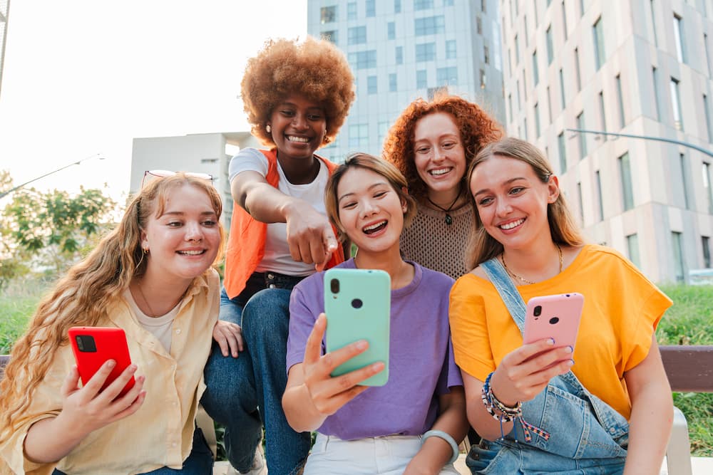 Symbolbild Gen Z und Alpha, lächelnde junge Menschen, die auf ein Smartphone blicken