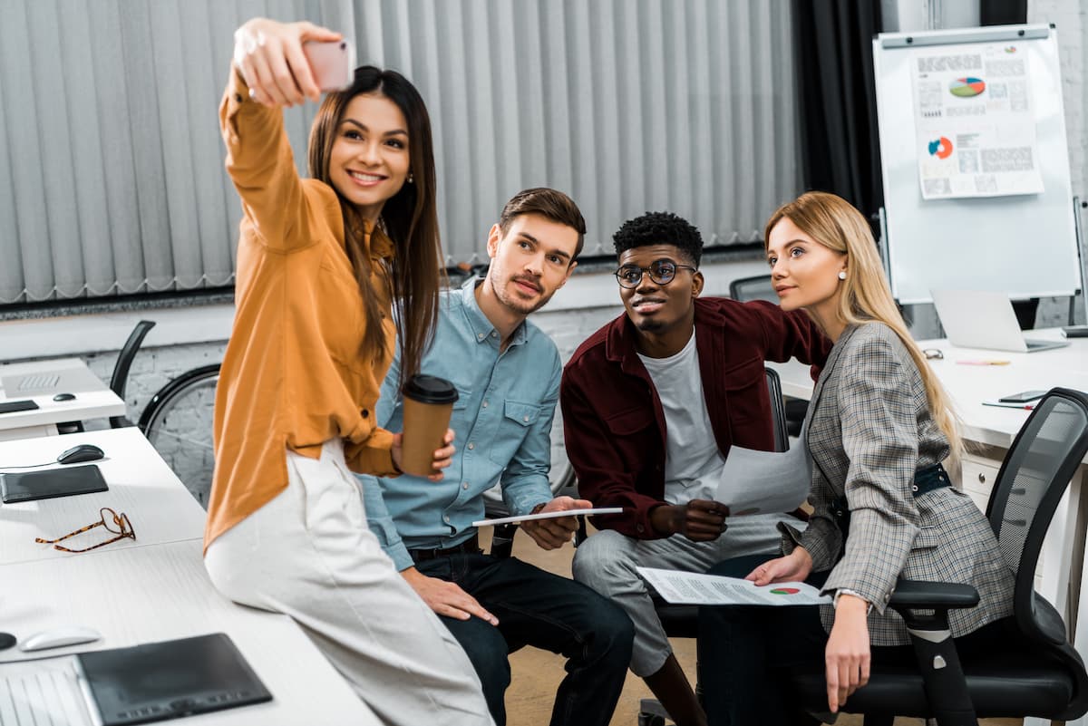 4 junge Kolleginnen und Kollegen sitzen im Büro und machen ein Selfie